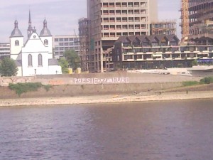 Rheinufer in Köln, an der Mauer gegenüber ist schwach der Schriftzug "Poesie du alte Hure" zu erkennen