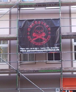 Werbebanner an einem Gerüst: Gerüstbau Systemfeind, dazu als Logo ein Totenkopf