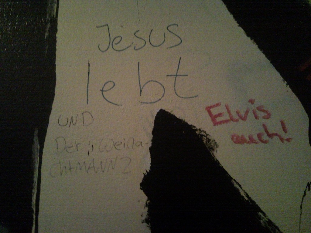 Detailaufnahme einer Hausflurwand, mehrere Schriftzüge: Jesus lebt, Elvis auch! Und der WeinachtMANN?