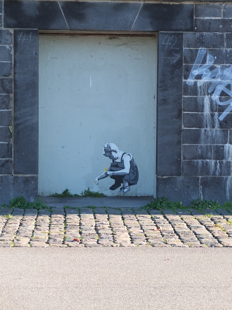 Street Art: Ein junges Mädchen sitzt in der Hocke und pflückt eine Blume