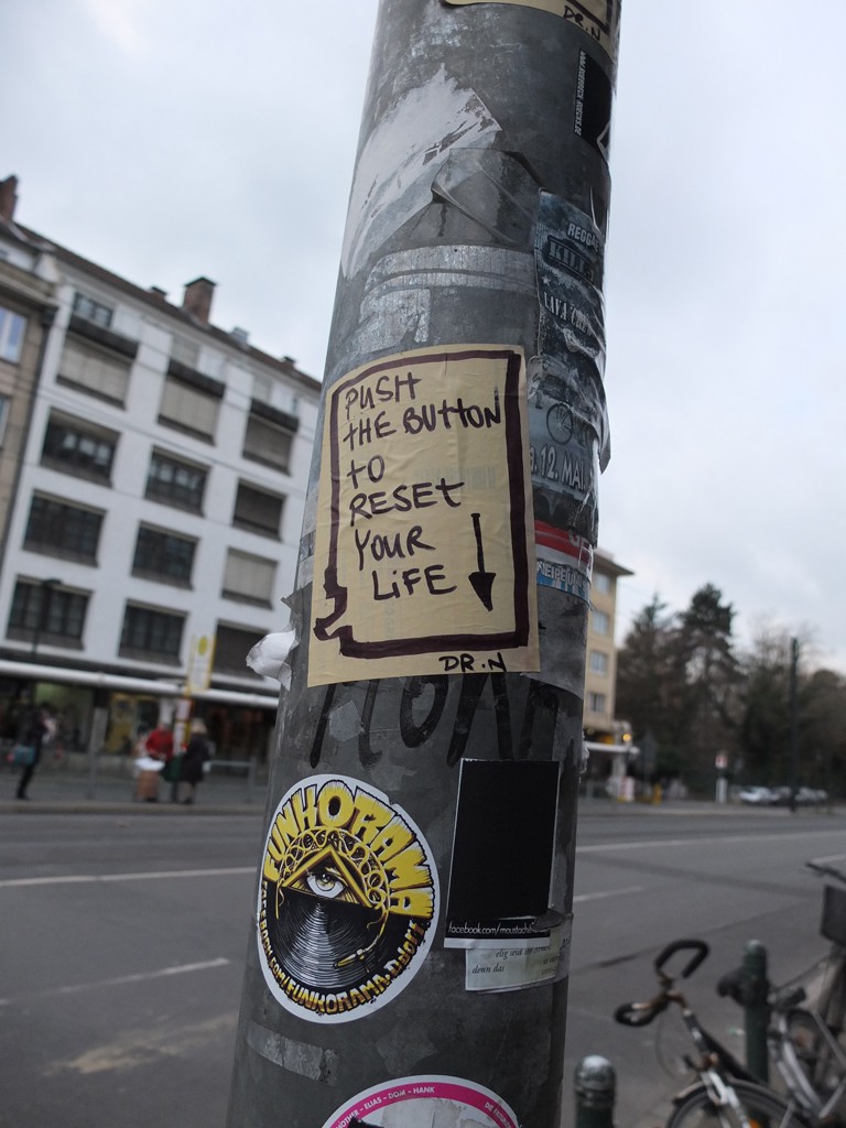 Street Art: Zettel an einem Ampelmast: Push the Button to reset your Life!