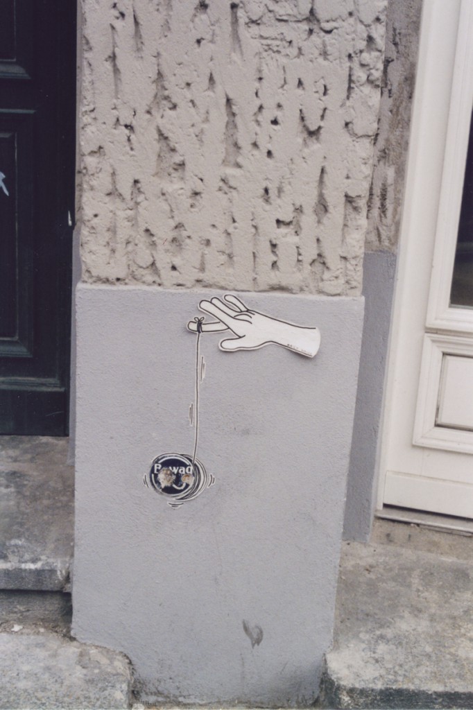Street Art Paste Up: Eine Bewag-Plakette dient als Jojo, der von einer Hand/den Fingerspitzen gehalten und bewegt wird