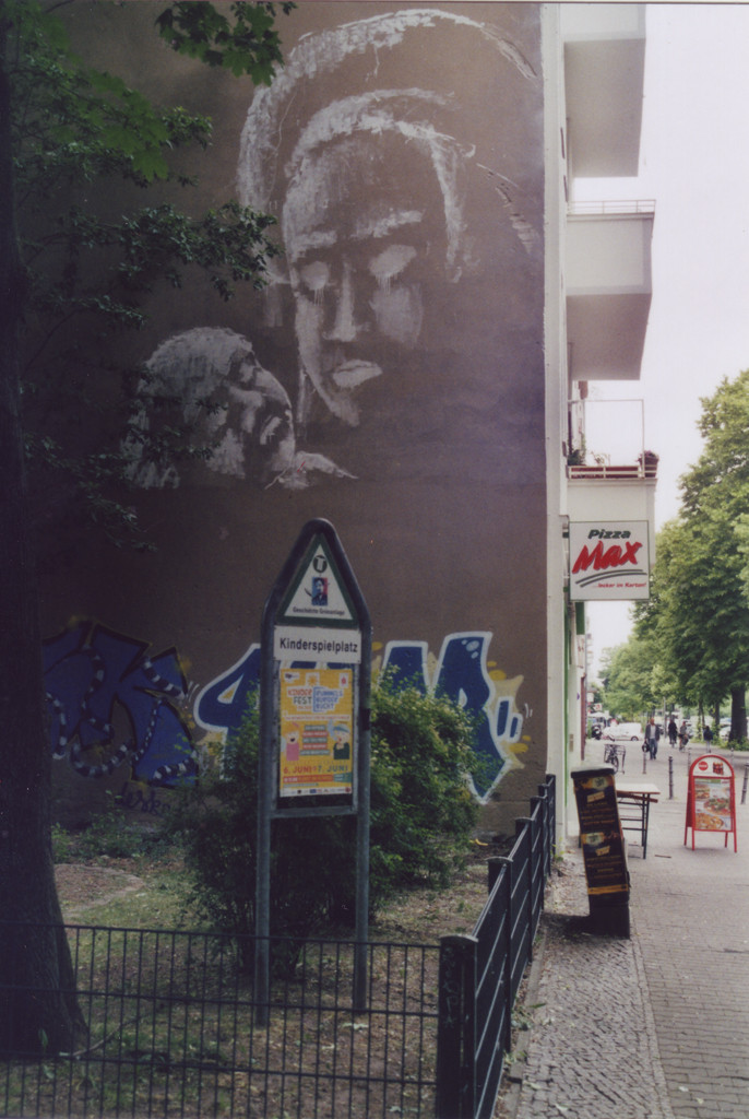 Wandbild an einer Brandmauer mit weisser Farbe: Silhouette einer Frau, die ein Baby in der Hand hält